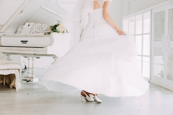 Beautiful attractive bride in wedding dress with long full skirt, white background, dance and smile - Foto, Imagen