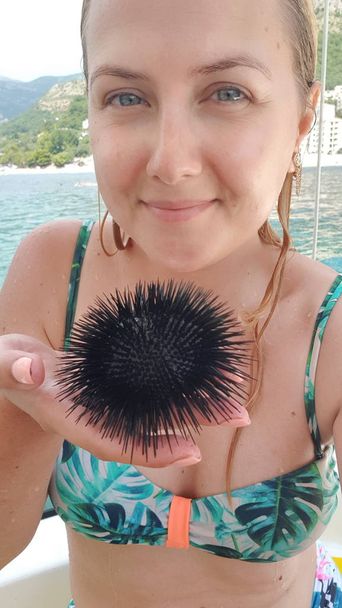 Jong meisje in een badpak houdt een zwarte zee-egels in de Palm van haar hand - Foto, afbeelding