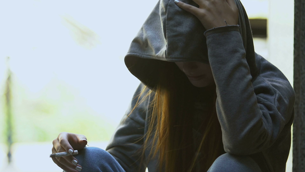 Mladá žena kouřící cigarety sedí venku, škodlivé návyky, puberta - Záběry, video