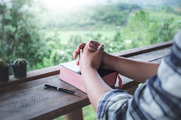 закройте руки человека, читающего и читающего по утрам священную Библию на деревянном столе. Концепция. - Фото, изображение