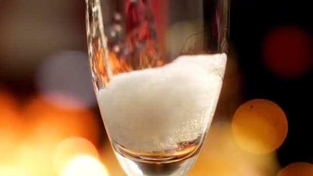 Macro slow motion video of pouring champagne from bottle in glass against glowing colorful lights. Gas bubbles and foam rising up. Perfect shot for parties,celebrations and holidays - Кадры, видео