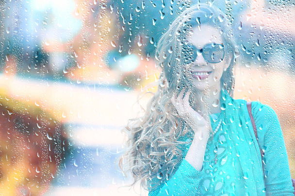 young adult girl outside the window view in the rain / raindrops on the glass warm autumn rain seasonal view - Foto, Imagen