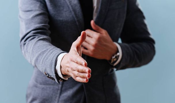 Businessman in suit extending hand, ready for handshake over blue background - Фото, зображення