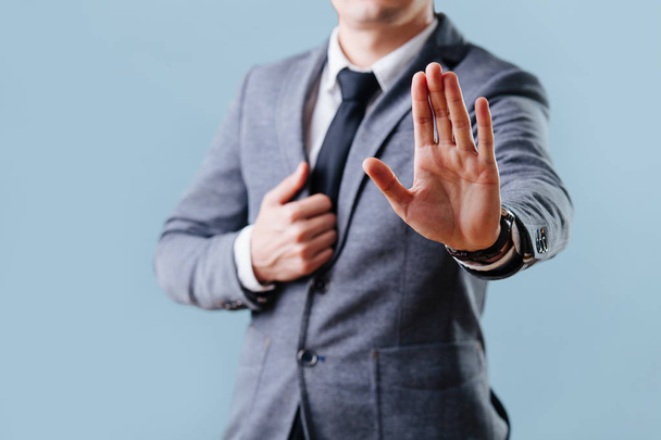 Businessman in suit making stop gesture, holding his palm outward over blue - Fotoğraf, Görsel