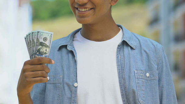 Happy teen boy showing bundle of dollars, money savings for dream, lottery win - Footage, Video