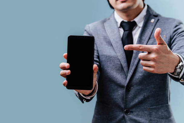 Бизнесмен показывает на свой смартфон указательным пальцем на синем фоне
 - Фото, изображение