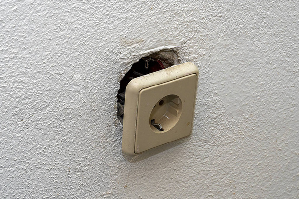 A dirty white socket fell out of the wall and hangs on wires. Repair in the house of old Euro sockets. - Φωτογραφία, εικόνα
