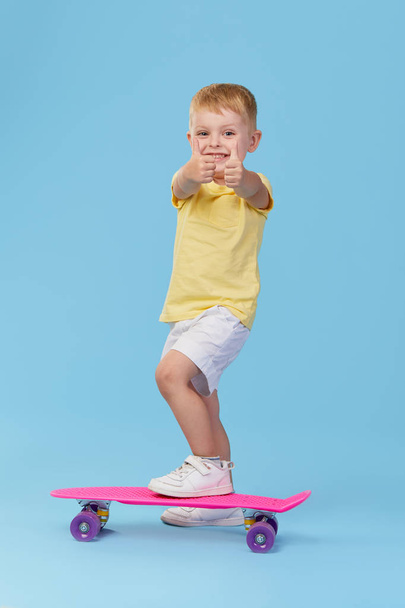 Stylish little toddler child boy in glasses with skateboard having fun over blue background - Photo, image