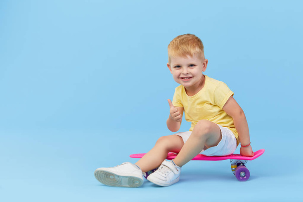 Stylish little toddler child boy in glasses with skateboard having fun over blue background - Foto, immagini