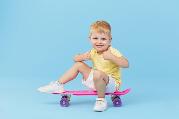 Stylish little toddler child boy in glasses with skateboard having fun over blue background - Photo, Image