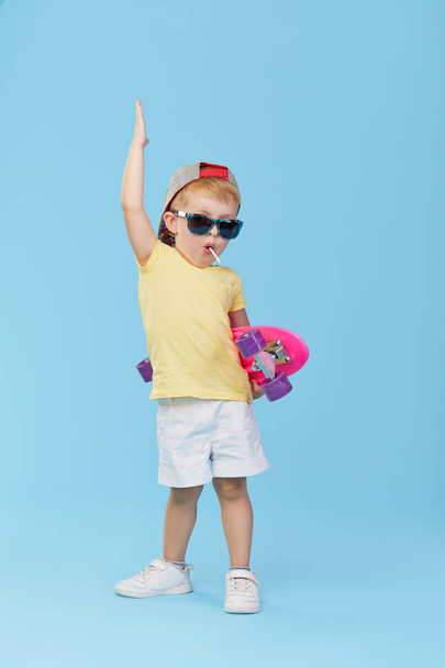 Stylish little toddler child boy in glasses with skateboard having fun over blue background - Foto, immagini