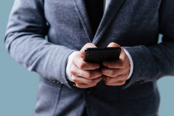 Empresário está digitando uma mensagem em seu smartphone sobre fundo azul
 - Foto, Imagem