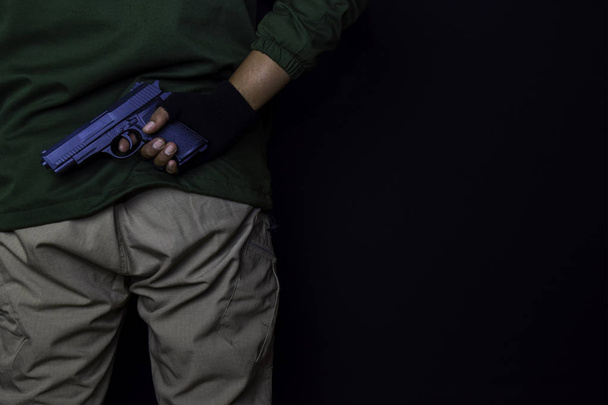 asian man holds a gun. Gun in his hand isolated on black background. - Foto, afbeelding