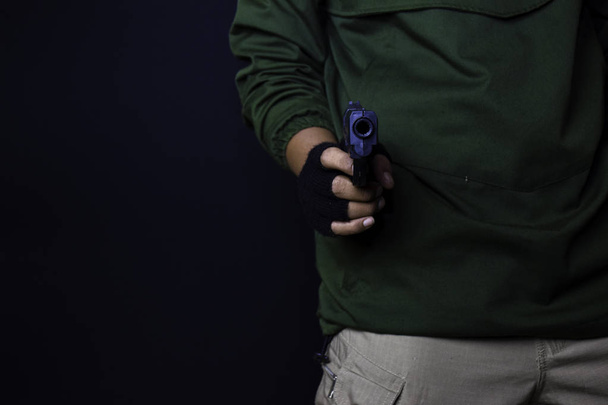 asian man holds a gun. Gun in his hand. Killed shooting his target isolated on black background. - Photo, Image