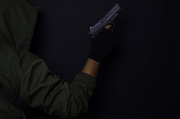 hombre asiático sostiene un arma. Pistola en su mano aislada sobre fondo negro
. - Foto, Imagen