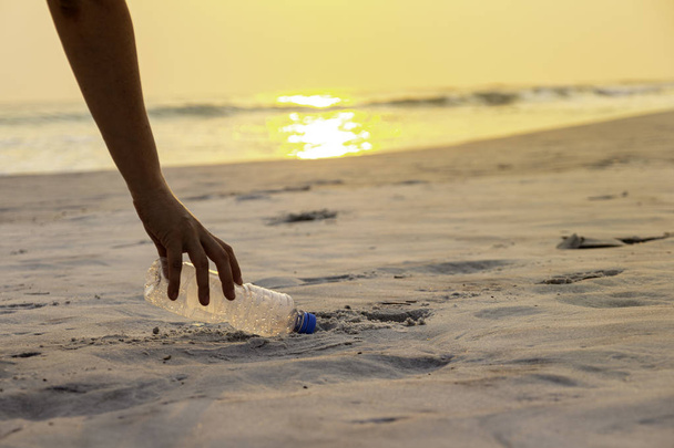 Ручна жінка бере пластикову пляшку для прибирання на пляжі, волонтерська концепція
. - Фото, зображення