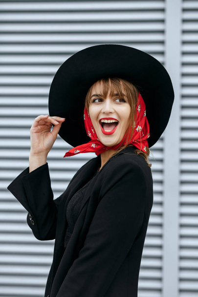 Menina alegre com lábios vermelhos usa traje preto e chapéu
  - Foto, Imagem