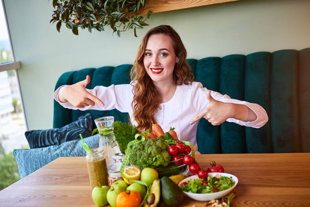 Woman dietitian in medical uniform with tape measure working on a diet plan sitting with different healthy food ingredients in the green office on background. Weight loss and right nutrition concept - Photo, Image