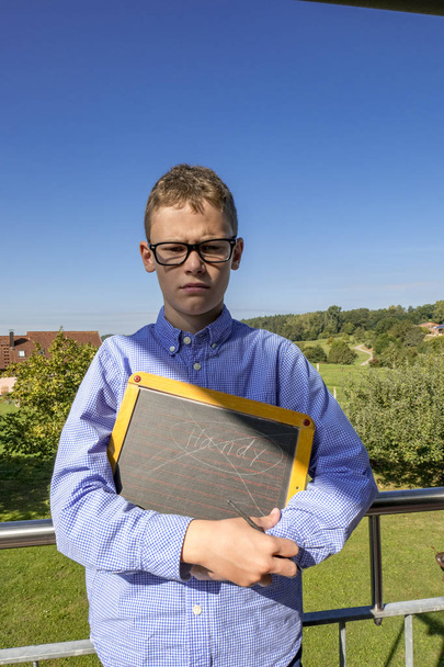 Mürrischer Junge mit Brille und blauem Hemd sieht arrogant aus, mit einer Tafel in der Hand - Foto, Bild
