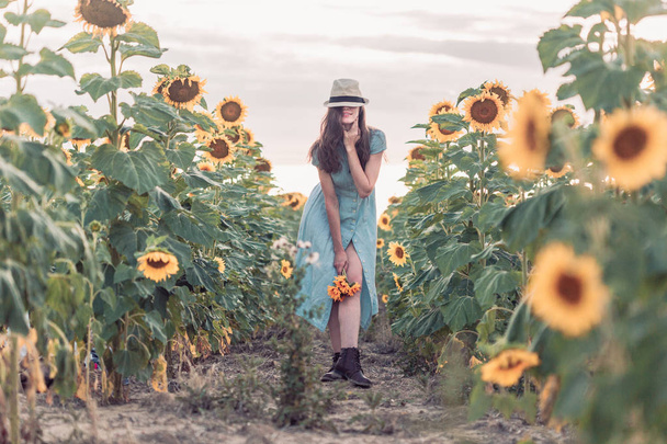 Mooie dame loopt op zonnebloem veld tijdens de zonsondergang in een zomer jurk. - Foto, afbeelding