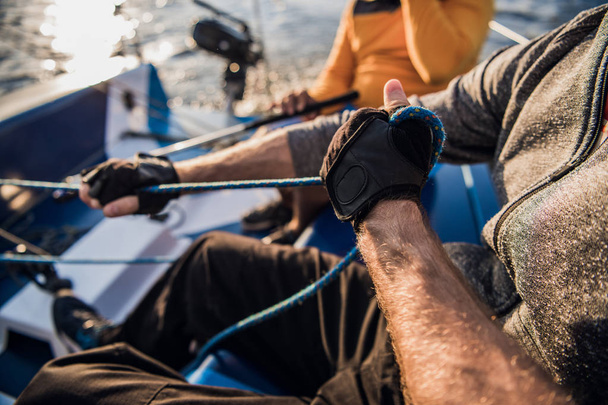 Männerhand mit Bootsseil. Segler legt sein Motorboot am Steg an. Hände und Bug des Bootes aus nächster Nähe. - Foto, Bild