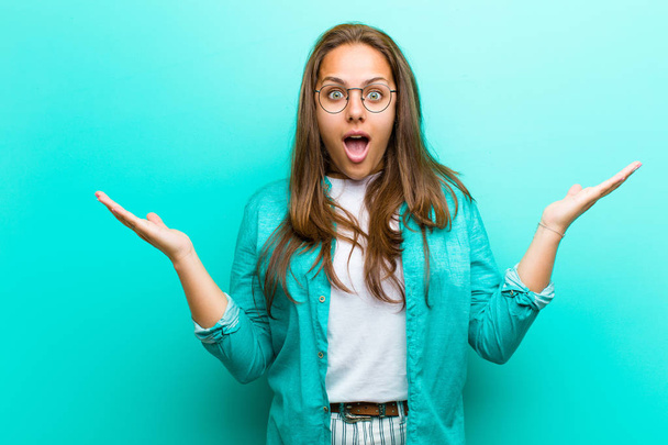 young woman feeling happy, excited, surprised or shocked, smiling and astonished at something unbelievable against blue background - Photo, Image