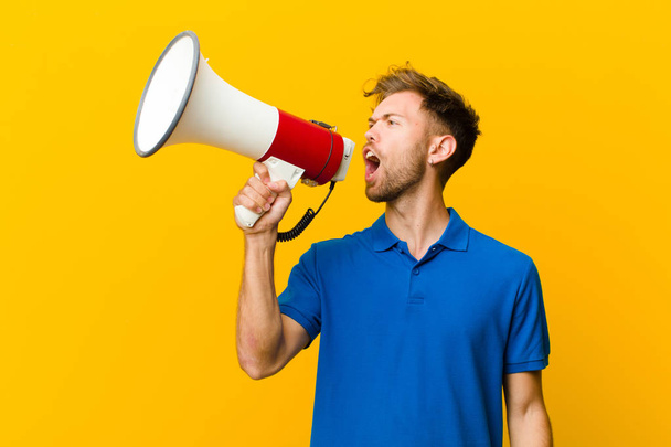 young man with a megaphone against yellow background - Fotó, kép