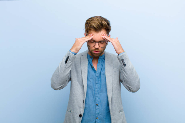 young businessman looking stressed and frustrated, working under pressure with a headache and troubled with problems against blue background - Foto, afbeelding