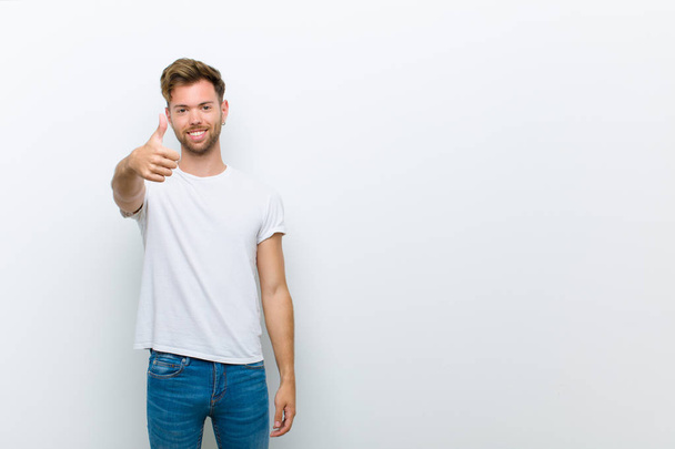 young man smiling and looking friendly, showing number one or first with hand forward, counting down against white background - Fotografie, Obrázek