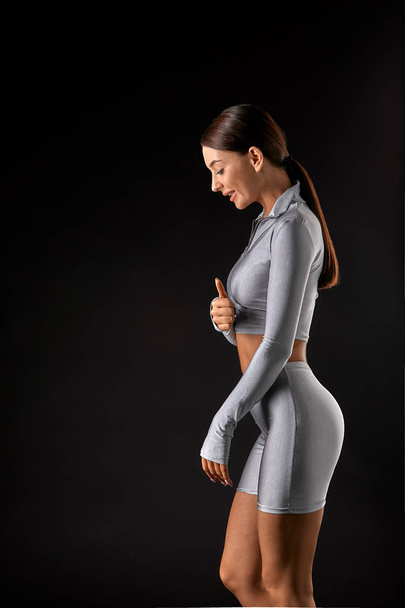 sexy brunette girl with a slim figure in leggings posing in studio on a black background - Fotó, kép