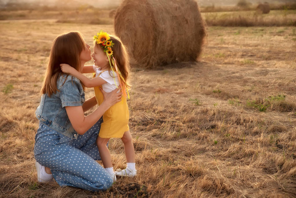 fröhliches Mädchen in gelbem Kleid umarmt junge Mutter im Herbstfeld - Foto, Bild