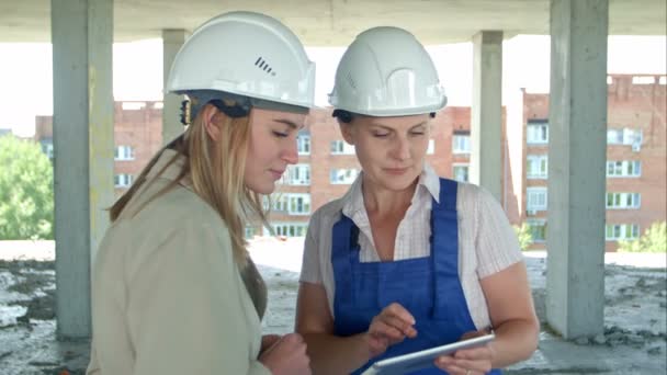 Female engineer and worker on construction site with plan on digital tablet - Footage, Video