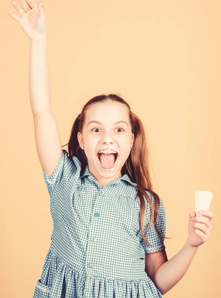 Happy childhood. Carefree kid enjoy sweet ice cream. International childrens day. Sweet tooth concept. Girl little child eat ice cream cone beige background. Summer is here. Delicious ice cream - Φωτογραφία, εικόνα
