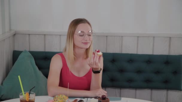 Beautiful young girl sits at a table in a cafe and eats sweet fresh desserts from a plate. - Filmagem, Vídeo
