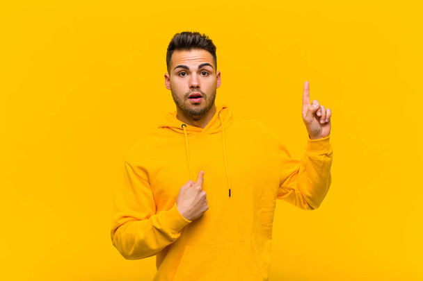 young hispanic man feeling proud and surprised, pointing to self confidently, feeling like successful number one against orange wall - Фото, зображення