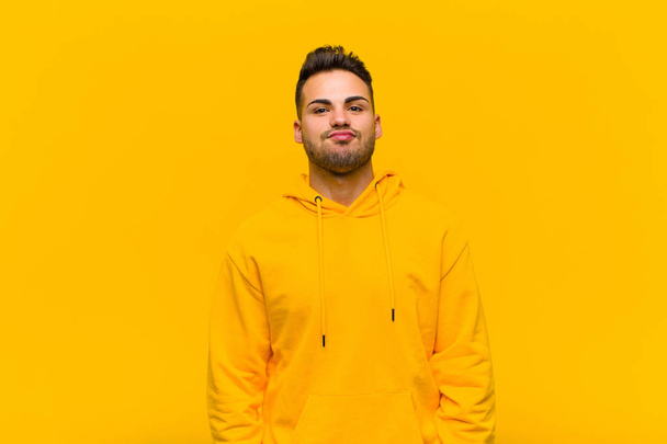 young hispanic man looking goofy and funny with a silly cross-eyed expression, joking and fooling around against orange wall - Foto, Imagen