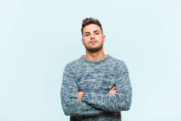 young hispanic man feeling displeased and disappointed, looking serious, annoyed and angry with crossed arms against blue background - Fotó, kép