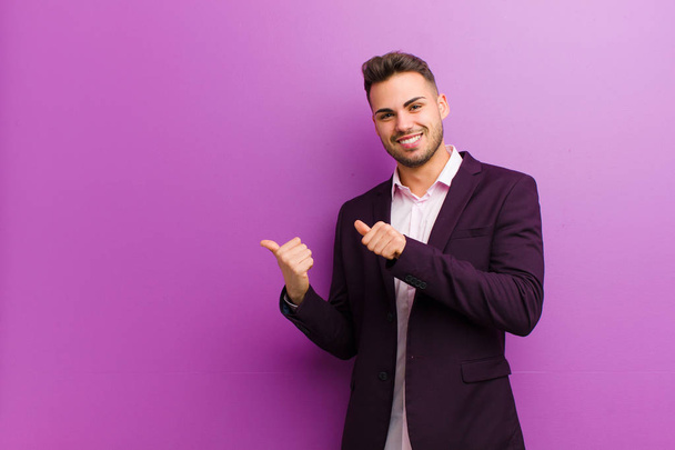 young hispanic man smiling cheerfully and casually pointing to copy space on the side, feeling happy and satisfied - 写真・画像