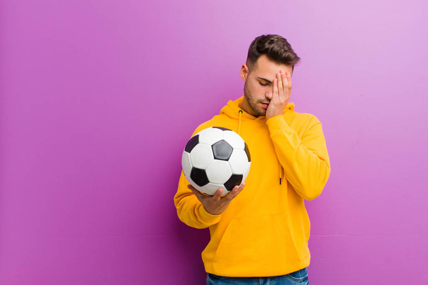 young hispanic man with a soccer ball against purple background - 写真・画像