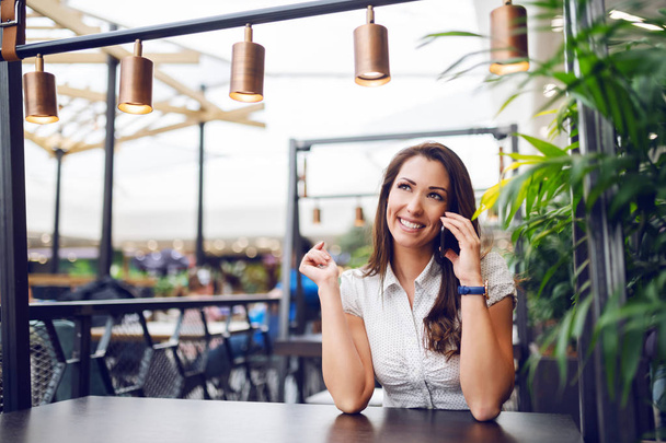 Portrét nádherné kavkazské brunetky sedící v kavárně v nákupním centru a drbající po telefonu. - Fotografie, Obrázek