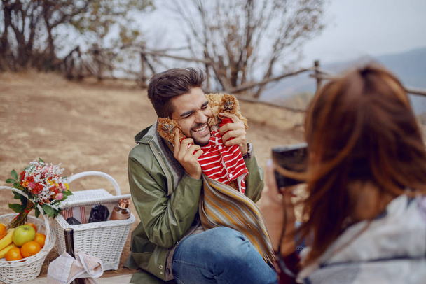Aranyos mosolygó boldog vegyes verseny férfi ül a takaró és pózol a kutya, míg a barátnője vesz képet róluk. Az őszi piknik koncepció. - Fotó, kép