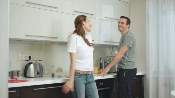 Joyful couple hugging each other at kitchen. Happy husband twisting smiling wife - Πλάνα, βίντεο