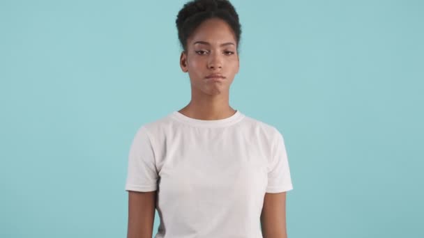 Egy feldúlt afro-amerikai lány arcképe, aki sajnálatos módon nem mutat gesztust, ahogy keresztezi egymás kezét a kék háttér felett. - Felvétel, videó