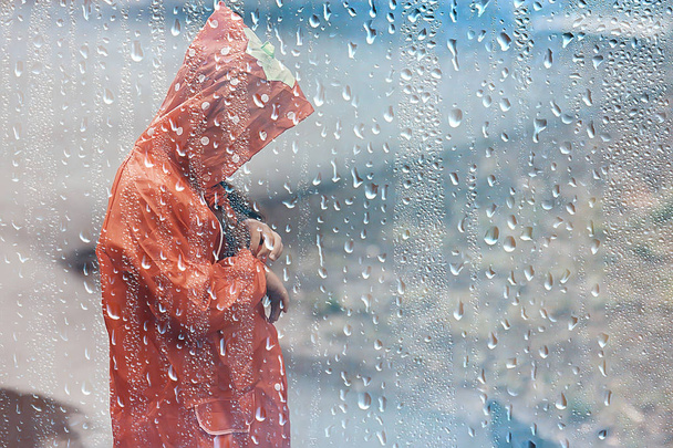 child in a raincoat plays outside in the rain / seasonal photo, autumn weather, warm clothes for children - Φωτογραφία, εικόνα