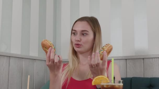 Beautiful girl posing with donuts in hands at a table in a cafe. - Imágenes, Vídeo