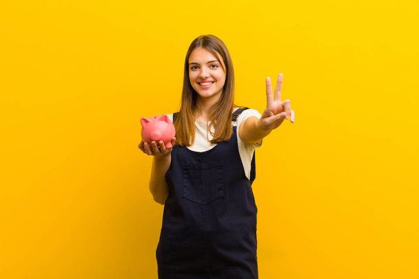 young pretty woman with a piggy bank  against orange background - Foto, imagen