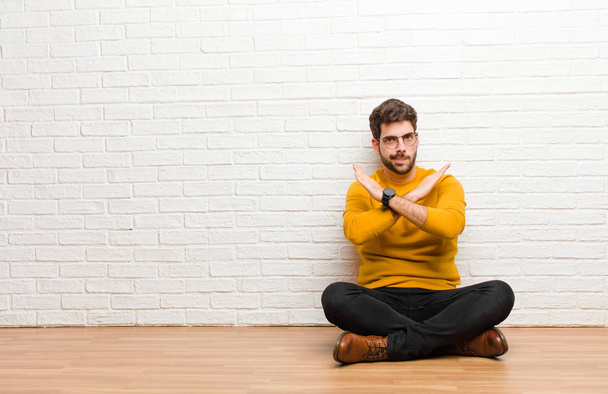 young handsome man sitting on home floor against brick wall texture - 写真・画像