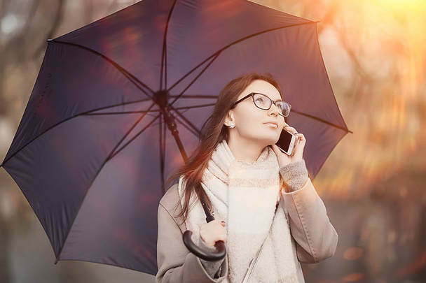 woman talking on the phone in the fall rain / autumn weather message about the rain, a model with an umbrella - Photo, image