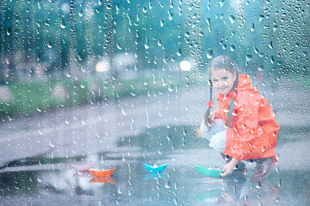 girl plays in paper boats in a puddle / autumn walk in the park, a child plays in the rain - Fotó, kép