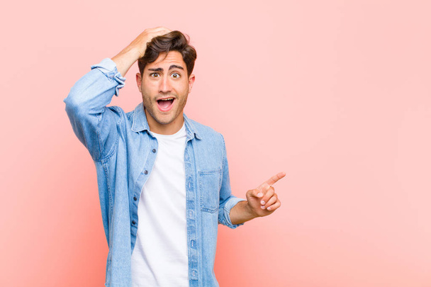 young handsome man laughing, looking happy, positive and surprised, realizing a great idea pointing to lateral copy space against pink background - Foto, imagen
